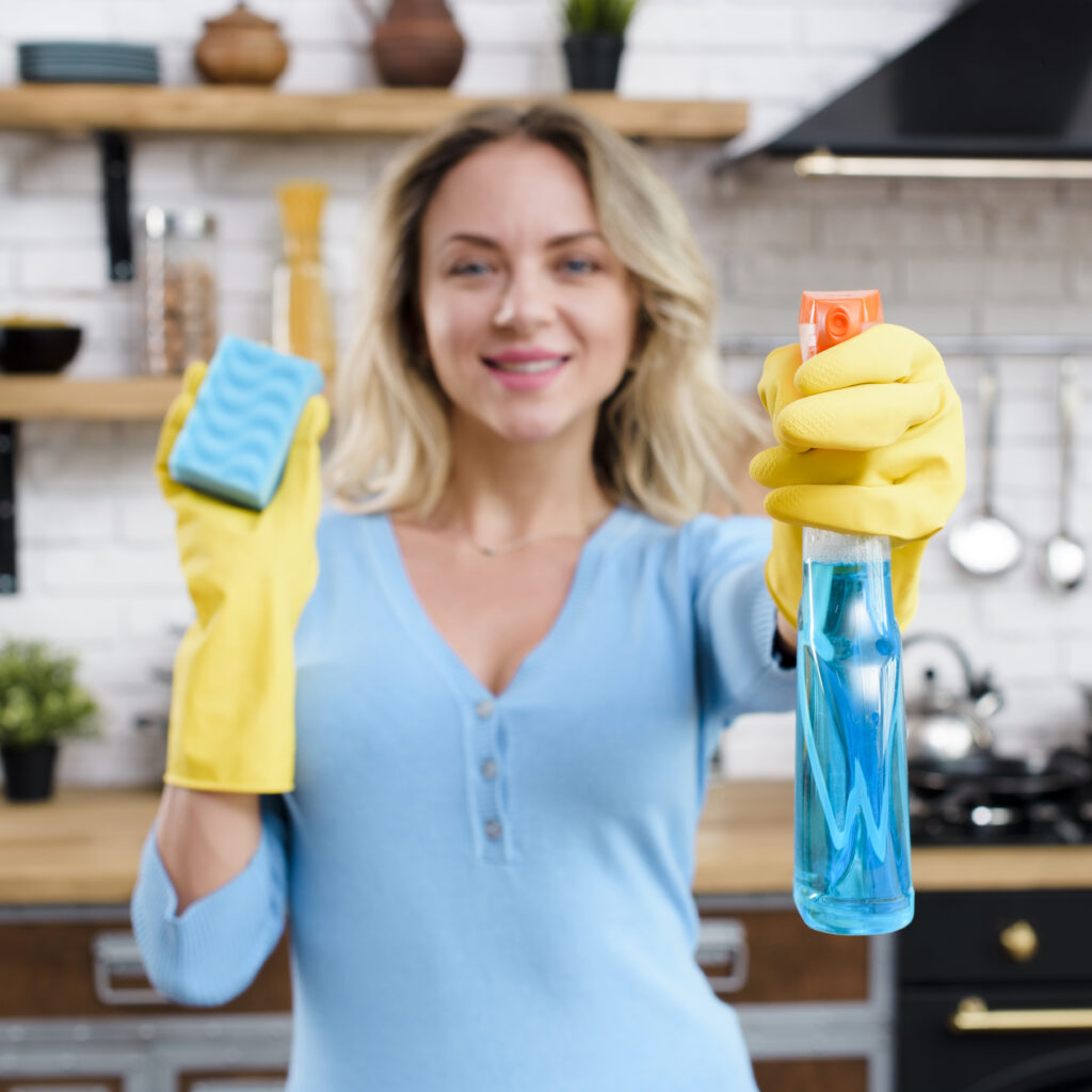 smiling-woman-wearing-rubber-gloves-holding-detergent-with-sponge